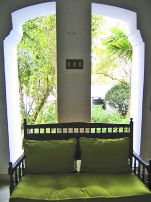 A wooden sofa with green cushions under an arch